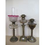 Three brass oil lamps, one with a cranberry tinted shade, wear to base, two lamps without shades,