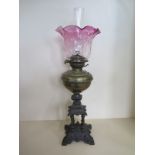 An oil lamp with cast iron base, brass font and cranberry tinted shade, 69cm tall including chimney