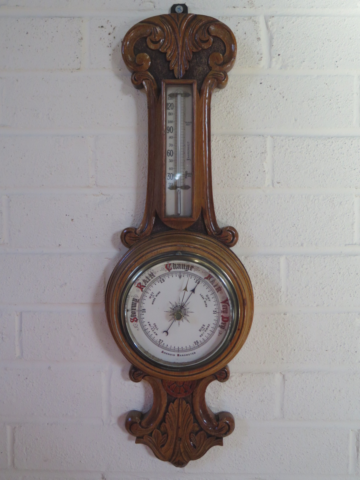 An carved oak case aneroid barometer with 5 inch white ceramic dial, approximately 59cm high, in