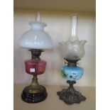 An oil lamp with a cranberry font and another with a decorated font, both 58cm H, both generally