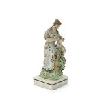 A Staffordshire figure of a shepherdess, c.1800, standing and tending a lamb which sits atop a