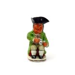 A Sinner Toby jug, c.1800, wearing a green jacket over a bold striped waistcoat, his warty face