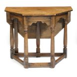 A 17th century style oak credence type table, the canted top with a hinged drop-leaf on a gate