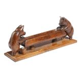 A treen pen tray, in the form of two pigs feeding at a trough, on an oak plinth, late 19th / early