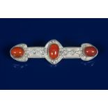 A Celtic Revival silver bar brooch, cast with simple geometric panels and set with three Carnelian