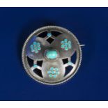 A silver and enamel brooch, circular with pierced panels, cast in low relief with blue enamel