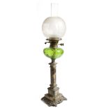 An Art Nouveau oil lamp, with a frosted glass globe shade, above a green glass reservoir, the