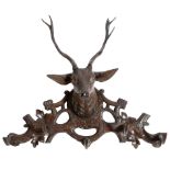 A late 19th century Black Forest carved and stained limewood stag's head coat hook, with glass