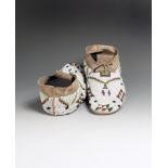 A pair of Plains moccasins buckskin and glass beads, fully beaded with a white ground and coloured