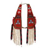 A Blackfoot horse crupper rawhide, red cloth, coloured glass beads, buckskin and brass bells, the