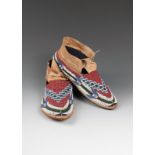 A pair of Cheyenne moccasins buckskin and coloured glass beads, fully beaded with a red ground to