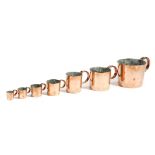 A harlequin set of seven copper navy rum or 'grog' measures, with loop handles, comprising: 1