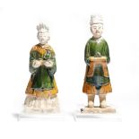 Two Chinese glazed pottery figures of attendants, wearing tunics, boots and hats and holding