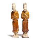 Two Chinese ochre glazed pottery figures, each wearing robes and sporting a headdress, Tang Dynasty,