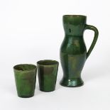 A Farnham Pottery Medieval jug and two beakers, the tall bellied jug with applied handle, covered in