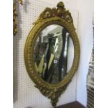 An oval gilt framed wall mirror with bevelled edge plate and moulded surround with raised