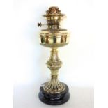 A Victorian polished brass oil lamp with fluted waisted column upon a polished black slate base