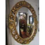 An oval gilt framed wall mirror with open scrolled acanthus and shell surround, 98 cm x 74 cam