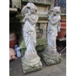 A matched pair of weathered cast composition stone garden figures in the form of classical maidens