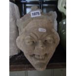 A carved natural stone corbel with female smiling/grimacing face mask wearing a crown/coronet 20