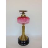 A 19th century brass oil lamp converted to electric, with cranberry glass reservoir upon a