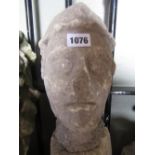 A small carved and weathered natural stone head of a male character wearing a brimmed cap and with