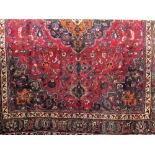 Persian Mashhad carpet, decorated with various orange and blue floral patterns upon a red ground