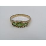 A three stone peridot ring in unmarked yellow metal, with scrolling decoration to the mount, size N,