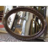 An oval Edwardian wall mirror with bevelled edge plate and moulded surround, pomegranate detail,