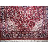 Persian wool rug decorated with various sky blue and white scrolled foliage upon a red ground, 200 x