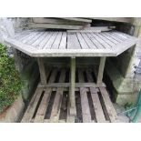 A weathered teak garden table with octagonal slatted panelled top raised on four rectangular cut