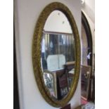 An oval gilt framed wall mirror with bevelled edge plate and moulded surround with scrolling