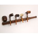 An oak wall mounted pipe rack in the form of a pipe - securing four pipes, all with silver mounts