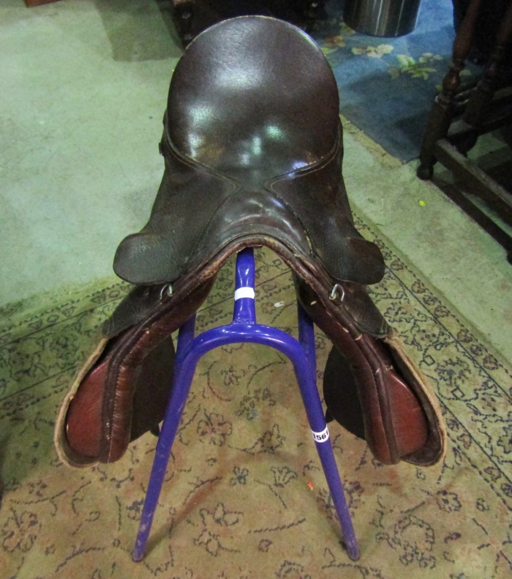 A stitched brown leather equestrian saddle, together with a tubular steel stand