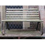 A two seat garden bench with weathered open hardwood slatted seat and combined back raised on a pair