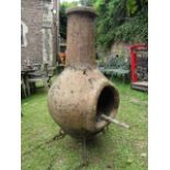 A large weathered contemporary clay chimenea with low ironwork stand, approx 4ft high including