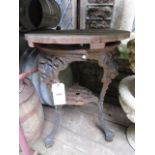 A cast iron pub table with female face mask and decorative pierced supports beneath a later