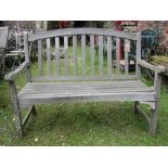 A weathered contemporary hardwood two seat garden bench with slatted seat and back beneath an arched