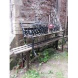 A small two seat garden bench with weathered wooden slatted seat and back raised on a pair of cast