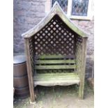 A stained and weathered pine framed arbour with open slatted bench seat and back within a lattice