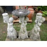 A weathered contemporary cast composition stone bird bath in the form of a seated cherub