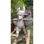 A weathered cast composition stone garden ornament in the form of a donkey carrying two simulated