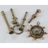 A yellow metal compass charm in the form of a ships wheel, together with a yellow metal watch key