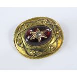 A cabochon garnet brooch set with a diamond in star cut surround, with trailing wirework border in