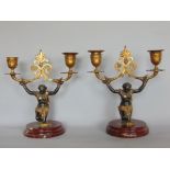 A good pair of French bronze and ormolu twin branch candelabra in the form of kneeling semi-nude