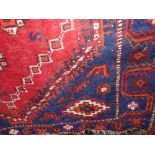 A Persian style wool rug with multi medallion detail upon a red field within alternating running