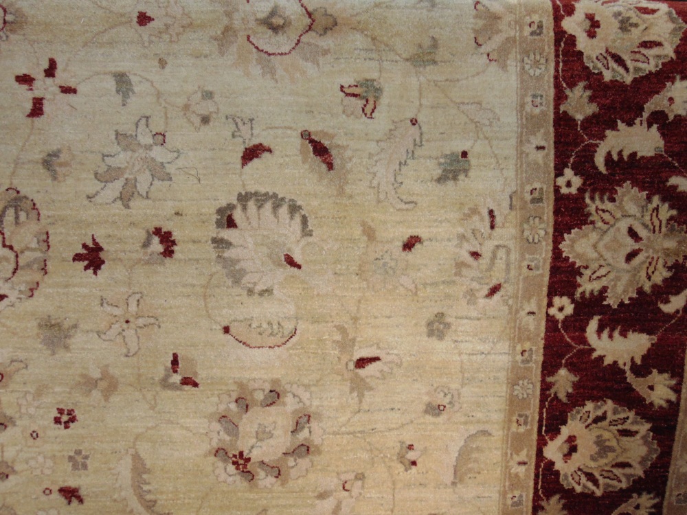 A large wool carpet in the Persian style, the pale cream field set within a burgundy coloured border