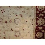 A large wool carpet in the Persian style, the pale cream field set within a burgundy coloured border