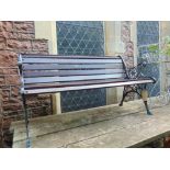 A small garden bench with carved and pierced iron work ends and timber lathes