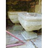 A pair of weathered reconstituted garden pots of square cut form on tapering stands and square cut